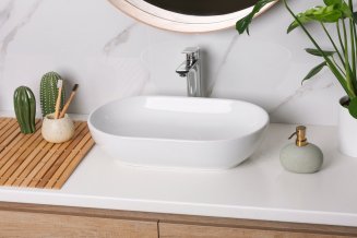 Ein modernes Waschbecken auf einem Waschtisch umgeben von Deko in Braun- und Grüntönen.